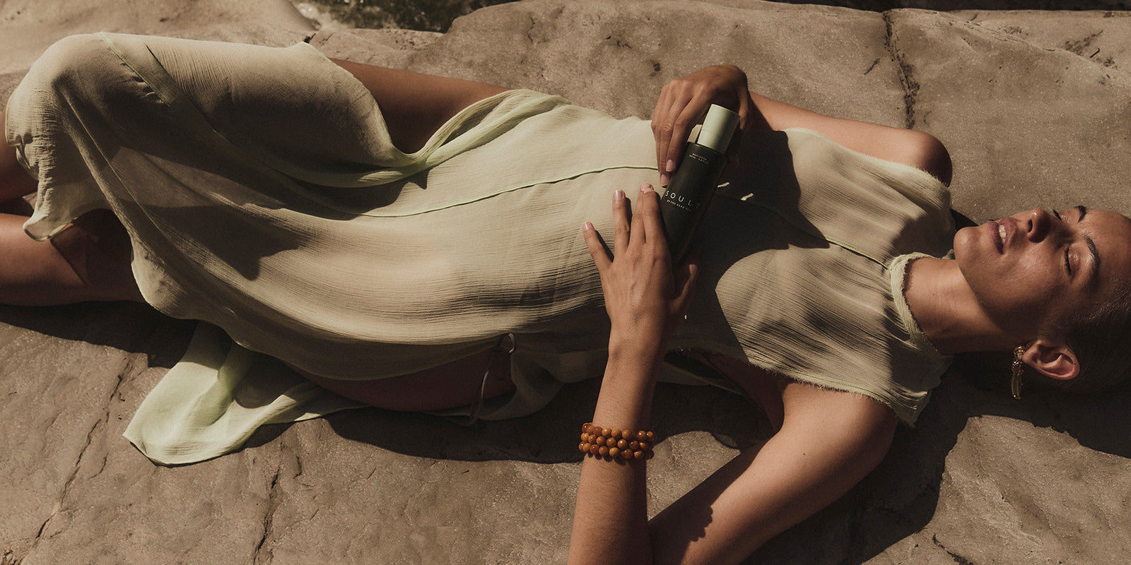 Woman laying on her back on stone with SOULT product in her hands